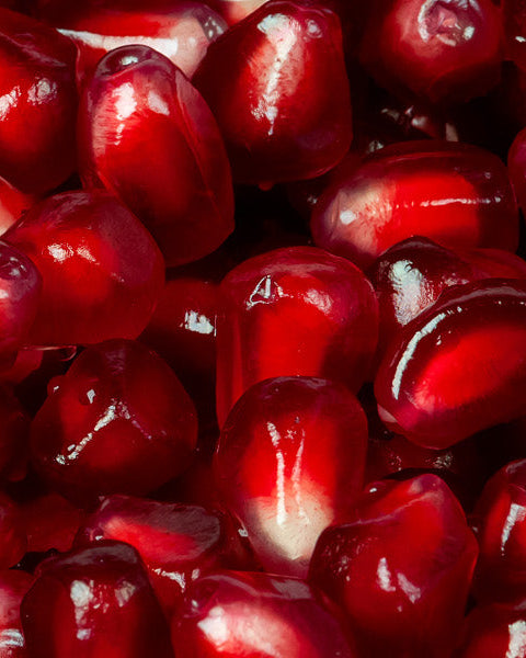 Vibrant ruby-red pomegranate seeds illustrating the tangy and bittersweet olfactory profile of raw perfume materials.
